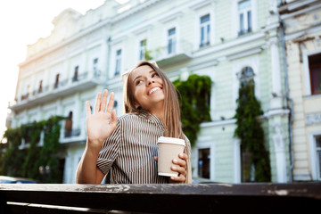 Fototapeta premium Young beautiful girl sitting on bench, holding coffee, smiling.
