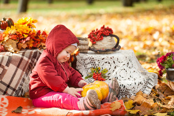 Small girl in autumn park playing with pumpkin