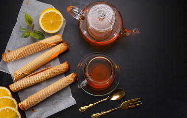 Waffle tubules with condensed milk and fresh hot tea and lemon over black background