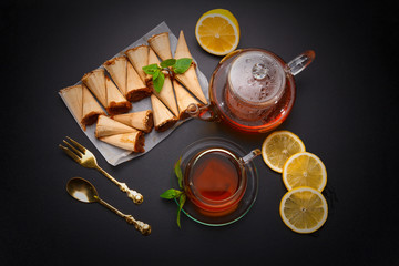 Homemade honey wafers rolled into a cone, filled with condensed milk, a cup of tea and lemon on a black table