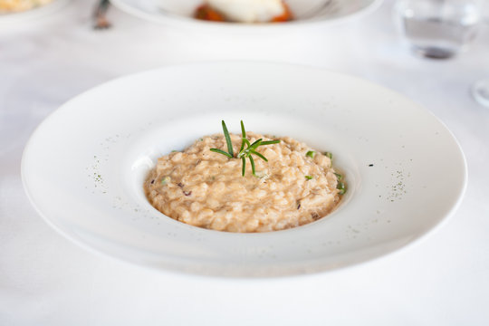 elegant circular bowl plate with rice in risotto and rosemary green leaf and chive pieces on white tablecloth in restaurant
