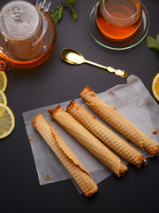 Waffle tubules with condensed milk and fresh hot tea and lemon over black background