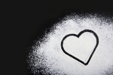 Flour and heart symbol. Flour on a black background.