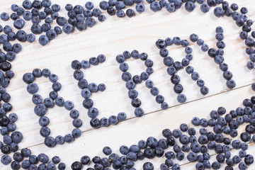 Word berry written letters with blueberries on white wooden boar