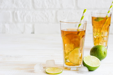 Ice tea in a glass with a slice of lime. White wooden plank back