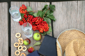 Naklejka na ściany i meble Red berries viburnum , green apples,bagels, a glass with water in it wooden background and river with blue clouds in it