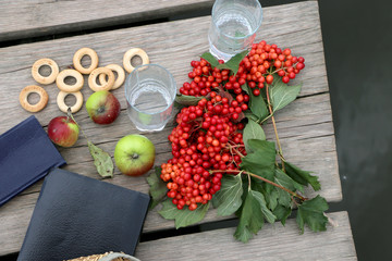 Red berries viburnum , green apples,bagels, a glass with  water in it wooden background and river with blue clouds in it