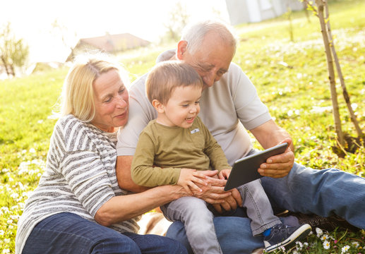 Grandparents with grandson enjoying the sunny spring day outdoors. They are looking something on tablet.