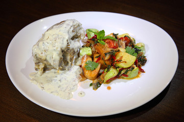 The dish is made from cow's tail, beautifully laid out on a plate with white sauce and vegetables.