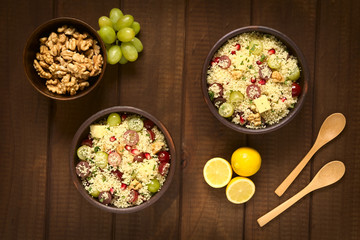 Frischer Couscous Salat mit Trauben, Granatapfel, Walnuss, Käse, Minze und Zitronensaft, fotografiert auf dunklem Holz mit natürlichem Licht