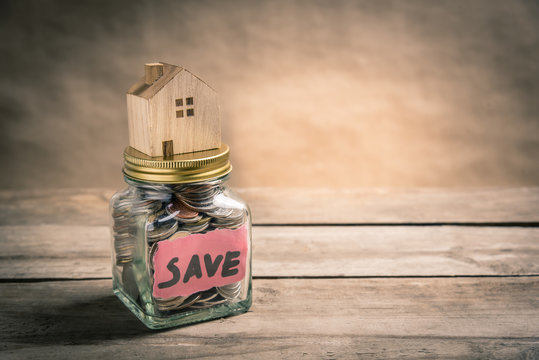Wooden house on jar of coins with the word save. Saving  concept. Vintage tone photo.