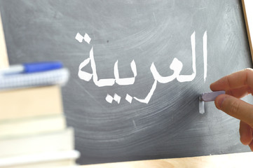 Hand writing on a blackboard in an Arabic class. Some books and school materials.