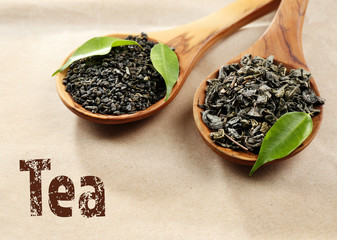 Dried tea with green leaves in wooden spoons on beige background.