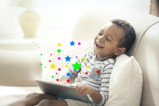 Cute little boy with digital tablet sitting on couch at home