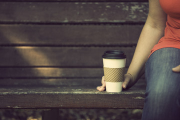 Woman sitting on wooden bench with take away coffee