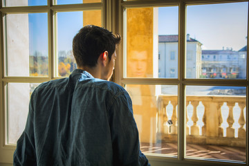 Fototapeta premium Half Body Shot of a Thoughtful Handsome Young Man Looking Away out of Window, Inside Historic Building in European City