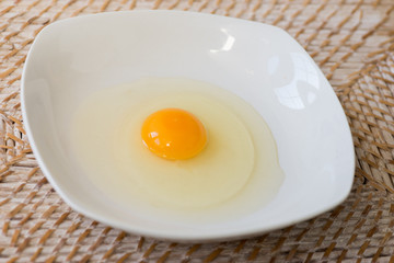 Raw egg on a white plate ready to get mixed with a fork