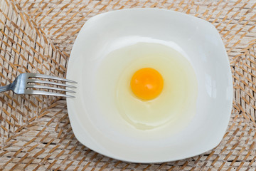 Raw egg on a white plate ready to get mixed with a fork