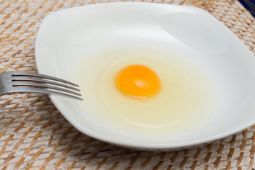 Raw egg on a white plate ready to get mixed with a fork
