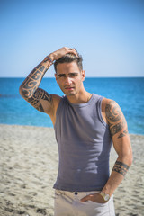 Three Quarter Shot of a Handsome Athletic Young Man in Trendy Attire, on a Beach in a Sunny Summer Day, Looking At Camera against Blue Sky Background.