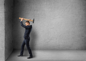 Side view of a businessman crashing concrete wall with hammer