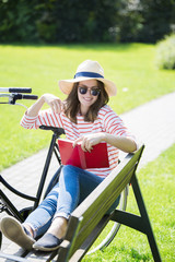 Full length portrait of a smiling beautiful young woman reading a book in the park. 