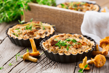 Homemade tarts of puff pastry with seasonal chanterelle mushrooms, cheese, thyme and onion on rustic wooden table - obrazy, fototapety, plakaty