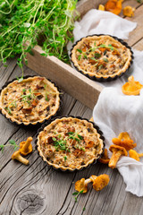 Homemade tarts of puff pastry with seasonal chanterelle mushrooms, cheese, thyme and onion on rustic wooden table, selective focus