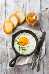 Pan of fried egg, crispy baguette and fruit jam on white rustic wooden table, top view. Breakfast time