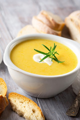 Delicious Vegetable cream soup in a white bowl and bread toasts on rustic wooden table, selective focus