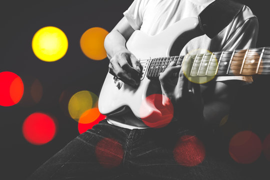 asian musician playing electric guitar with colourful bokeh light on stage