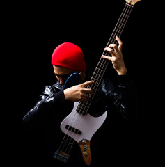 asian professional musician in leather jacket, red hat playing electric bass guitar, isolated on black