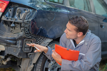 Mechanic holding clipboard assessing car