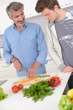 Man preparing vegetables, younger man looking on dubiously