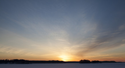 Amazing and colorful sunset in the winter time in Finland. Image taken on a lake and the forest far away is a silhouette.