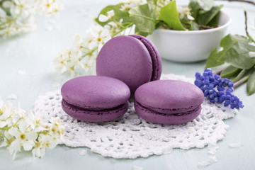 Fototapeta na wymiar Three purple macaroons cookies and flowers on the table