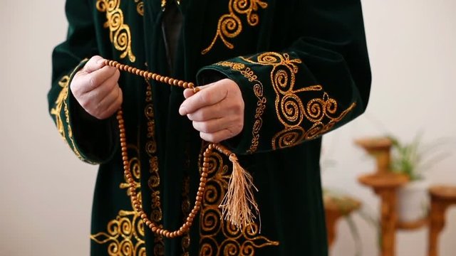 An old mullah in national dress praying with rosary beads in hands. Slow motion