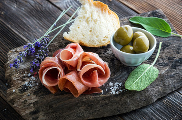 Prosciutto with olives on wooden background