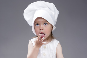 Cooking Concepts and Ideas. Portrait of Lovely Cute Caucasian Girl Posing as Little Cook in Cap. Against Gray