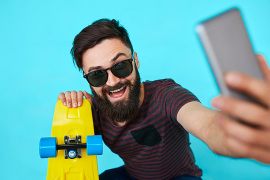 Young hipster with beard in glasses taking selfie and smiling isolated on the blank white background