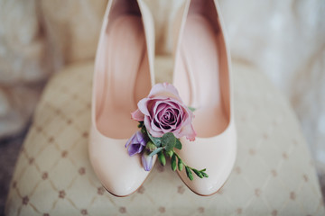 Shoes of the bride standing next to the groom's buttonhole of flowers and greenery