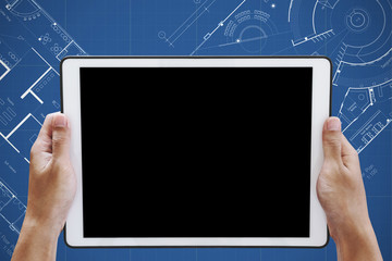 Hand holding digital tablet with copy space on screen, on architectural blueprint background