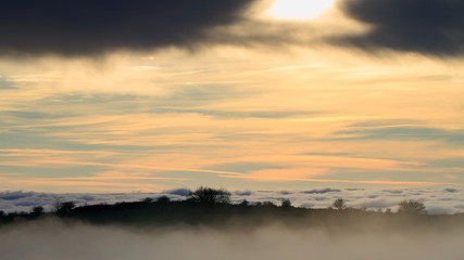 Landscape with the sun setting behind clouds and fog