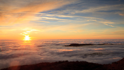Landscape with the sun setting behind clouds and fog