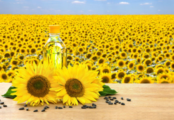 Bottle of sunflower oil with flowers and seed of sunflower on wooden table on background blossoming field of sunflowers