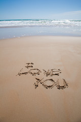 i love you text written on brown sand ground low tide beach ocean seashore in Spain Europe
