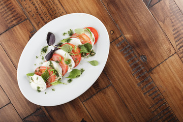 Salad with Mozzarella and tomato in white oval plate. wooden background.