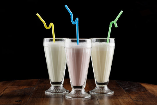 Milk shake (cocktail) with berry and banana in glass on brown wooden table