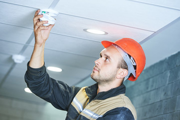 worker installing smoke detector on the ceiling