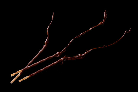 Knusprige Sticks mit geschmolzener Schokolade auf schwarzem Hintergrund